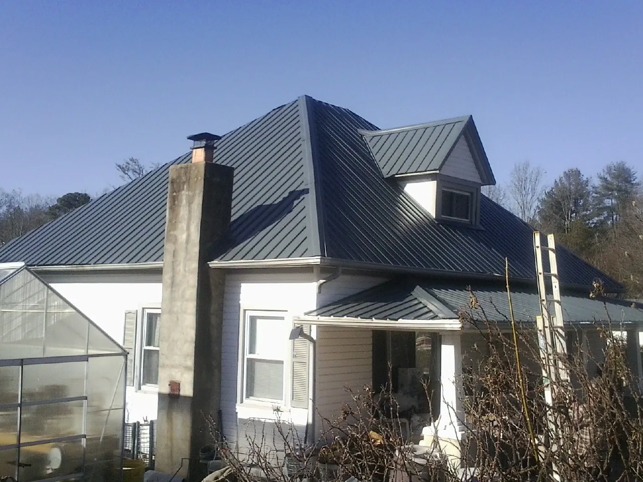Dark blue standing seam metal roof on a white farmhouse with dormer — Slate & Tile Roof Repair by Roofing Brothers in Locust Grove