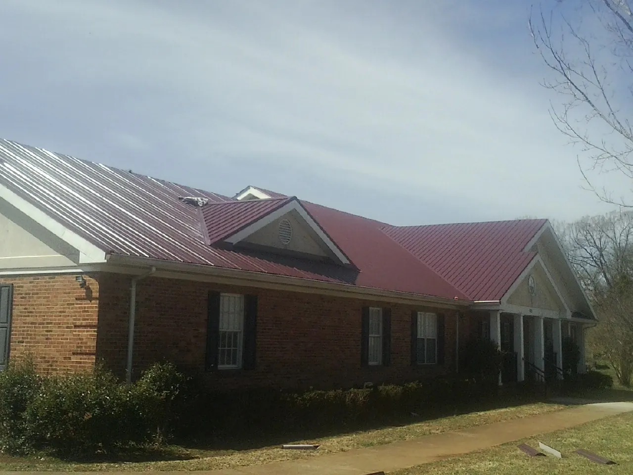 Red metal roof with gabled entries on a long brick building, from a Hail Damage Roof Repair job in Locust Grove