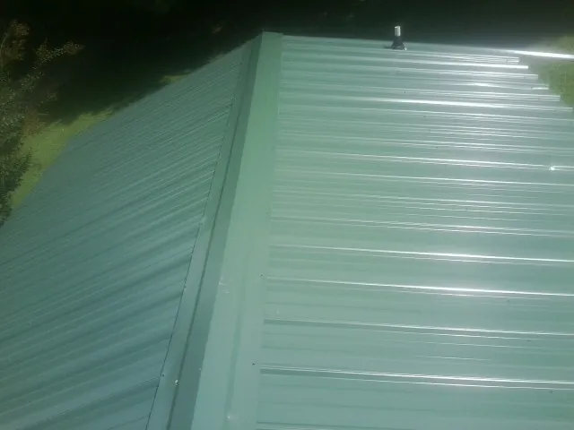 New green metal panels meeting at the ridge of a roof — Flat Roof Repair work by our crew in Locust Grove
