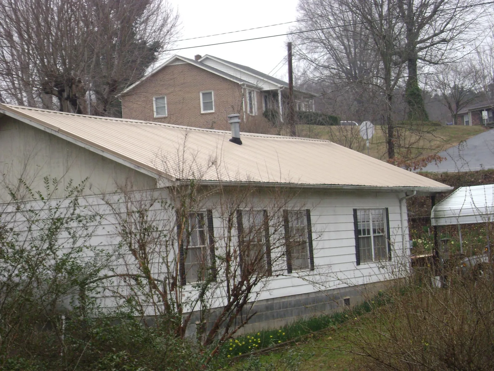 Tan metal roof on a white sided house set into a hillside — Commercial Roofing by Roofing Brothers in Locust Grove