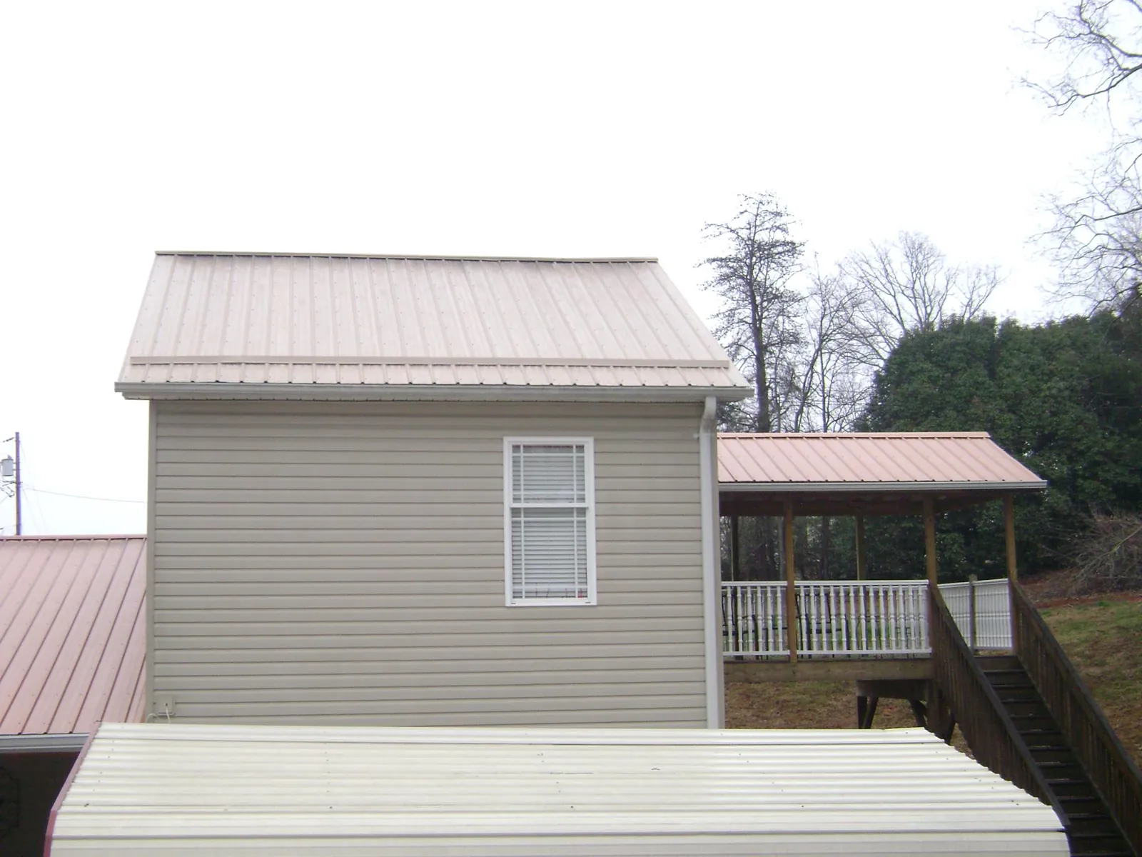 Tan metal roofs on a two story addition and attached porch, from a Roof Replacement job in Locust Grove